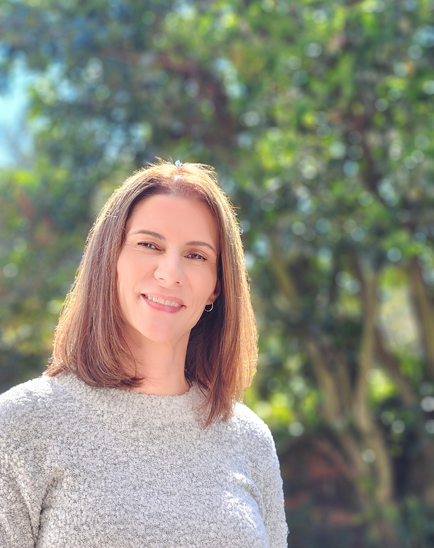 Claire, coach for women in midlife, smiling in a park in soft afternoon light